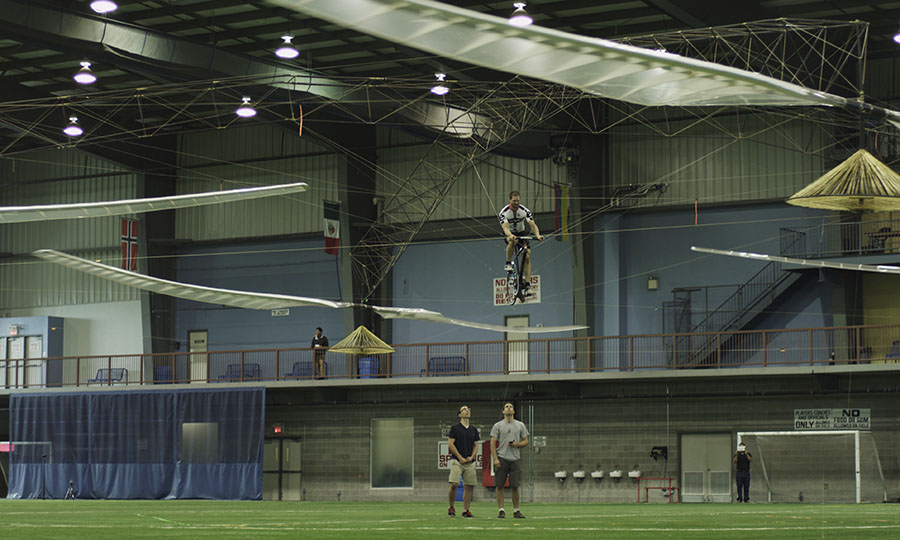 Pilot pedals helicopter above the ground crew at indoor soccer field.
